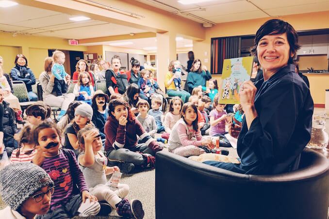 At a book event in the before-times, where I handed out moustaches to each guest. The kid in the front is putting one on their forehead - brilliant!