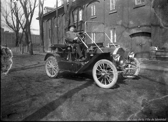 1910?-Employé des travaux publics asssis dans une voiture stationnée devant un bâtiment de l'aqueduc