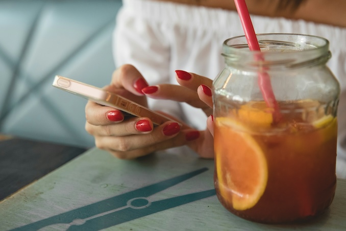 Woman using a cellphone at a table with a glass of juice in front of her.